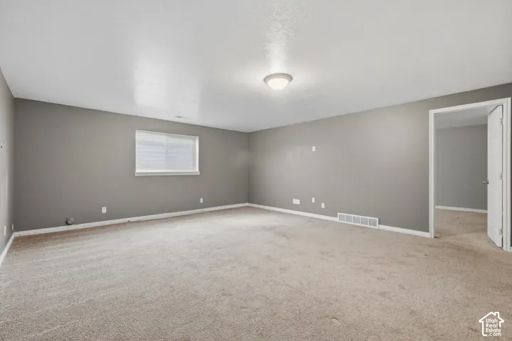 Spacious room featuring carpet flooring, neutral gray walls, a single window, and ceiling-mounted lighting