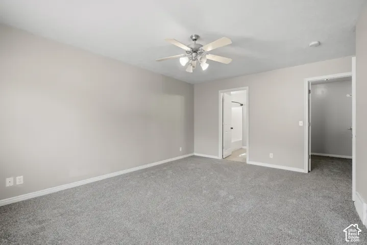 Spacious room featuring neutral carpeting, light-toned walls, a ceiling fan with integrated lighting, and white trim