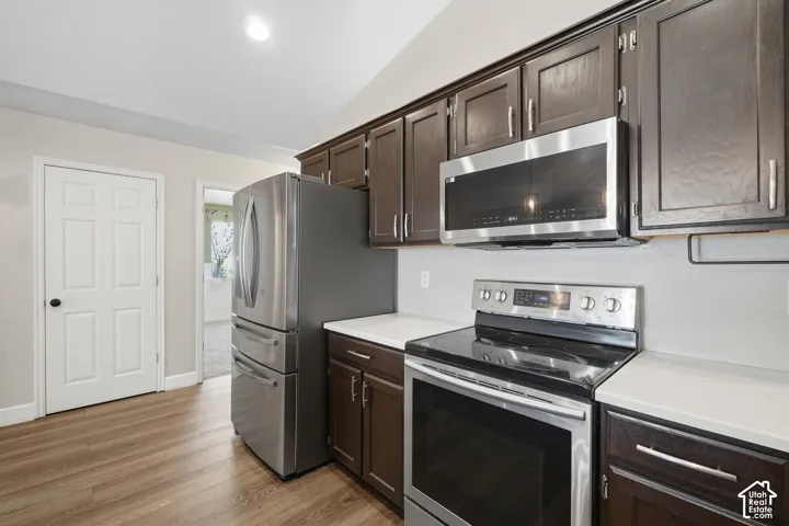 Wood-finish flooring, dark wood cabinetry, white countertops, and stainless steel appliances, including an electric range and microwave