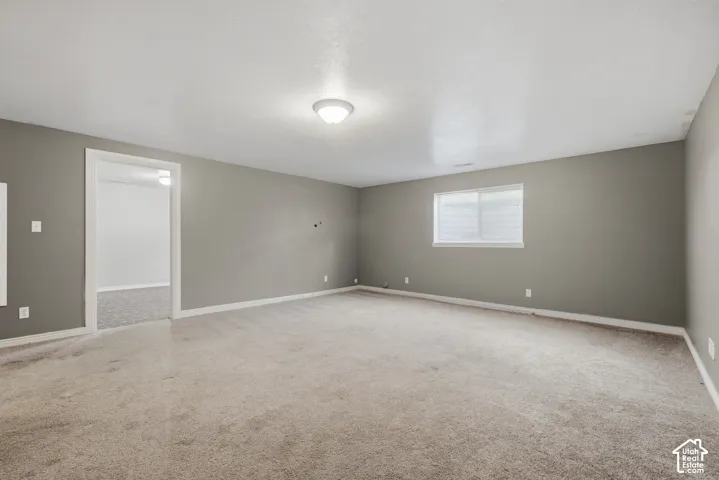 Spacious room with neutral gray walls, beige carpet, overhead flush-mount lighting, and a single window