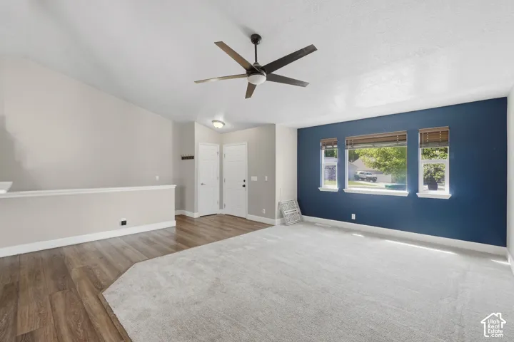 Vaulted ceiling with a ceiling fan, wood-finish flooring, and carpeted floor area