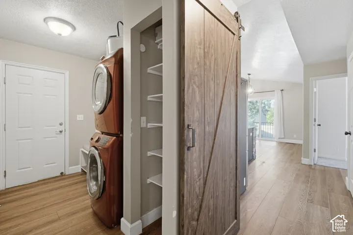 Wood-finish flooring throughout, integrated laundry area with a stacked washer and dryer, adjacent pantry with built-in shelving, and a wood barn door