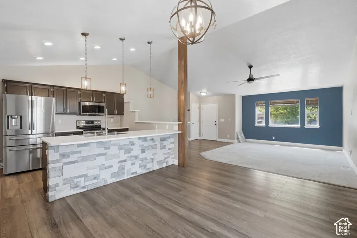 Vaulted ceilings with a decorative chandelier and ceiling fan, wood-finish flooring, and a kitchen island with a stone-clad facade