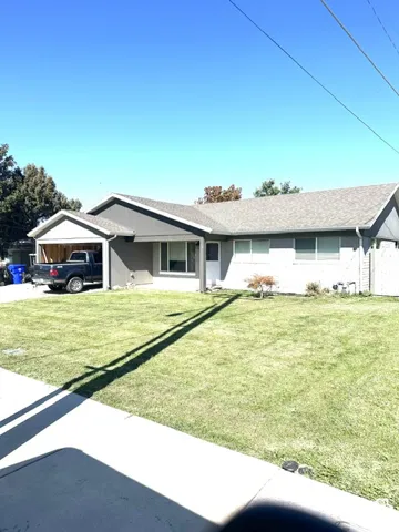 Light-colored stucco exterior with a gray-toned shingle roof, offering a covered carport and an attached garage