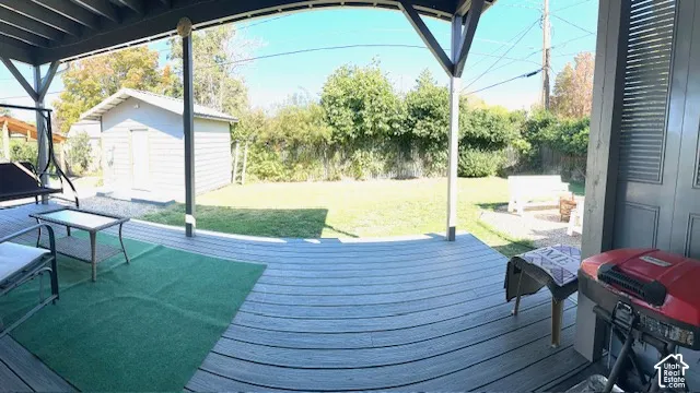 Covered outdoor deck with composite decking, expansive backyard lawn, detached shed, and fenced perimeter