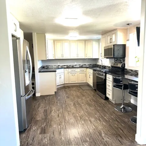 White cabinetry, dark stone countertops, wood-finish flooring, stainless steel appliances, and a tiled backsplash