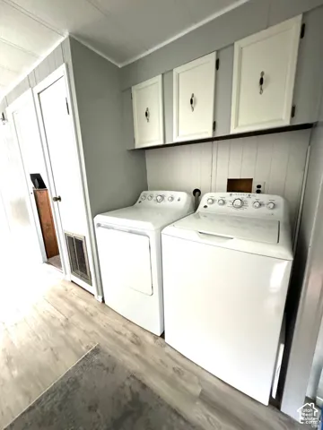 Laundry area featuring wood-finish flooring, overhead cabinetry, and white shiplap paneling