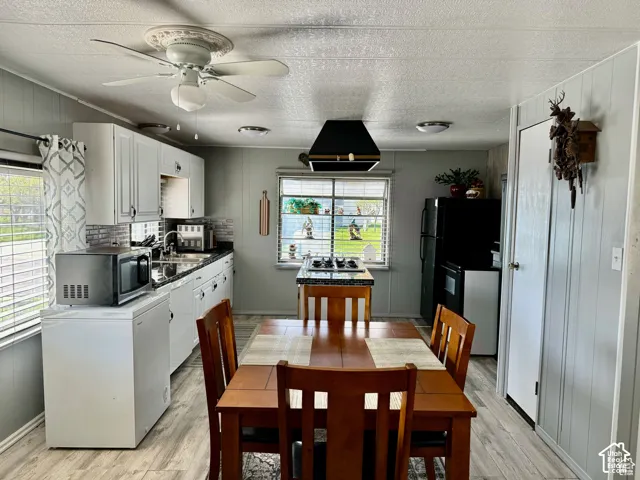 White upper and lower cabinetry, wood-finish flooring, a ceiling fan with light, and a black appliance suite