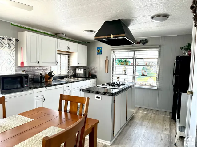Kitchen featuring white cabinetry, dark countertops, a tiled backsplash, a kitchen island with a built-in cooktop, and wood-finish flooring