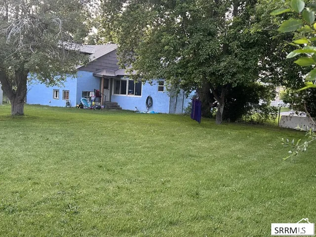 Expansive lawn area with mature trees, a blue-painted exterior, and a metal roof