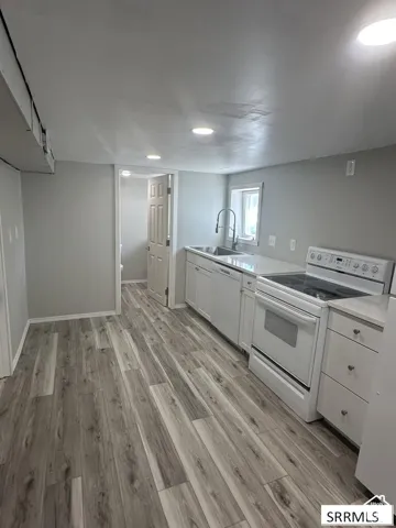Wood-finish flooring, recessed ceiling lighting, white cabinetry, integrated stainless steel sink, and a white electric range