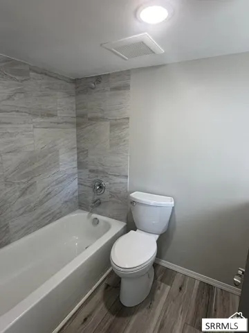 Bathroom featuring a white bathtub, chrome shower fixtures, a white toilet, and wood-finish flooring