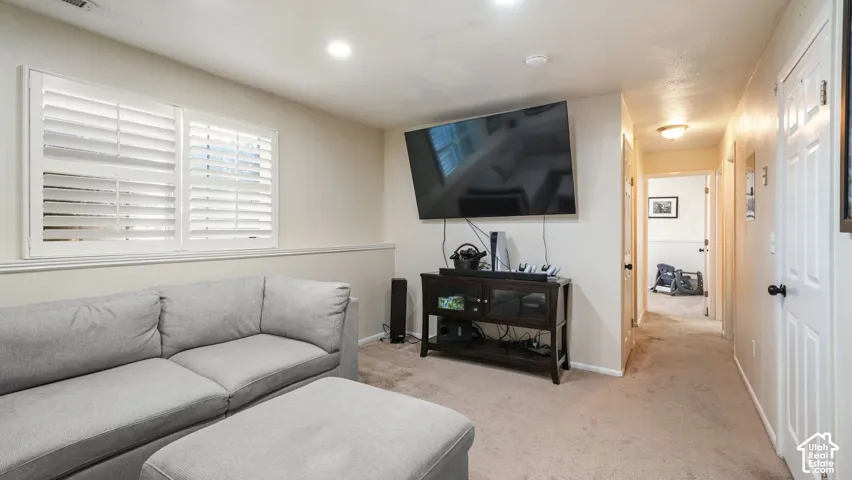 White plantation shutters, recessed lighting, wall-mounted television, wood-finish media console, and neutral carpet flooring