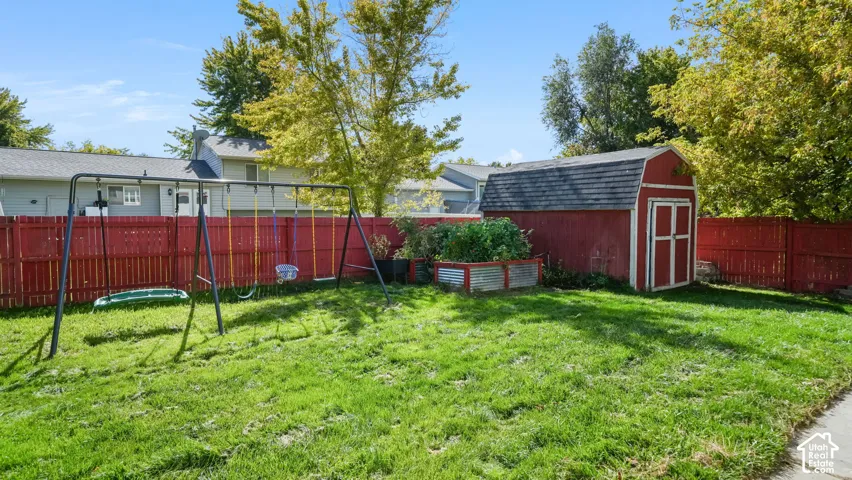Expansive grassy yard area featuring a red wooden fence and a red storage shed with a gambrel roof