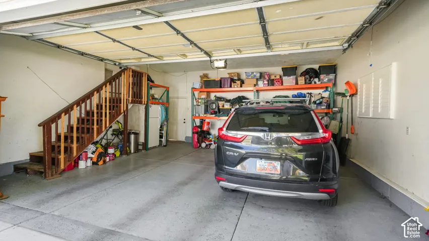 Attached garage space featuring a wood-finish staircase and ample shelving for organization