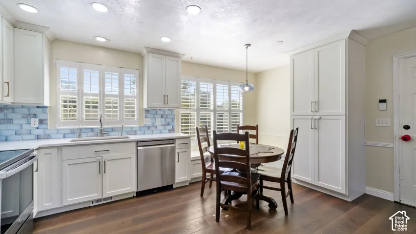 White shaker-style cabinetry, stainless steel dishwasher, white countertops, blue-toned subway tile backsplash, and wood-finish flooring