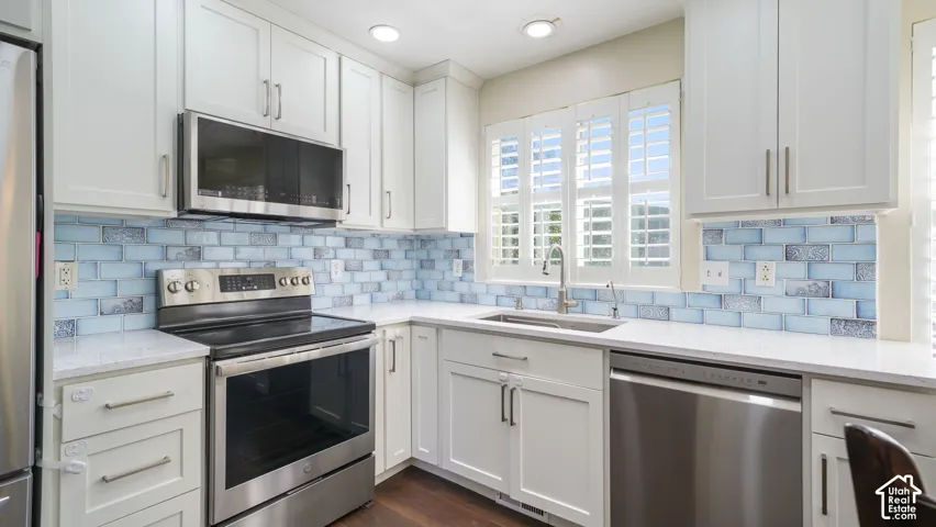 White shaker-style cabinetry, stainless steel appliances, light-toned countertops, and a blue tile backsplash