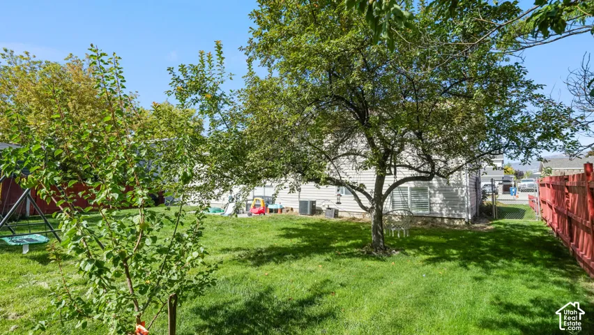 Expansive backyard featuring mature trees, a red privacy fence, and a manicured lawn
