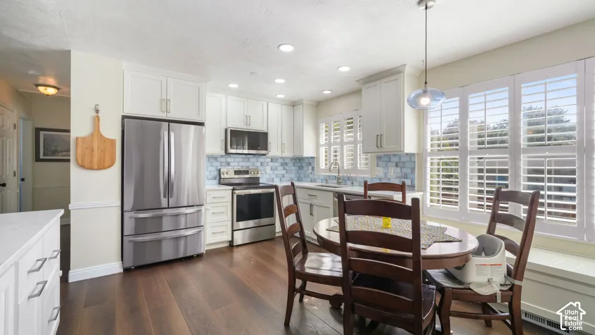 Kitchen featuring white cabinetry, stainless steel appliances, wood-finish flooring, a light blue tile backsplash, and plantation shutters
