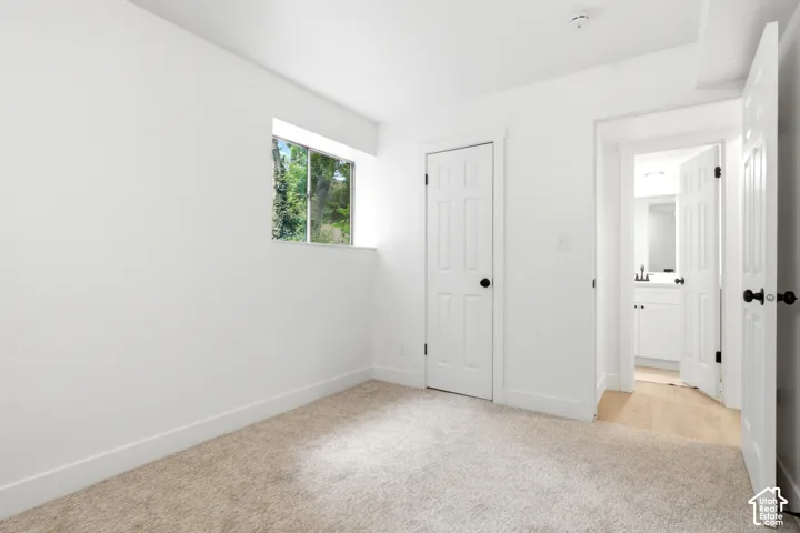 Light-colored carpeting with white baseboards, white walls, and a single window with exterior greenery visible