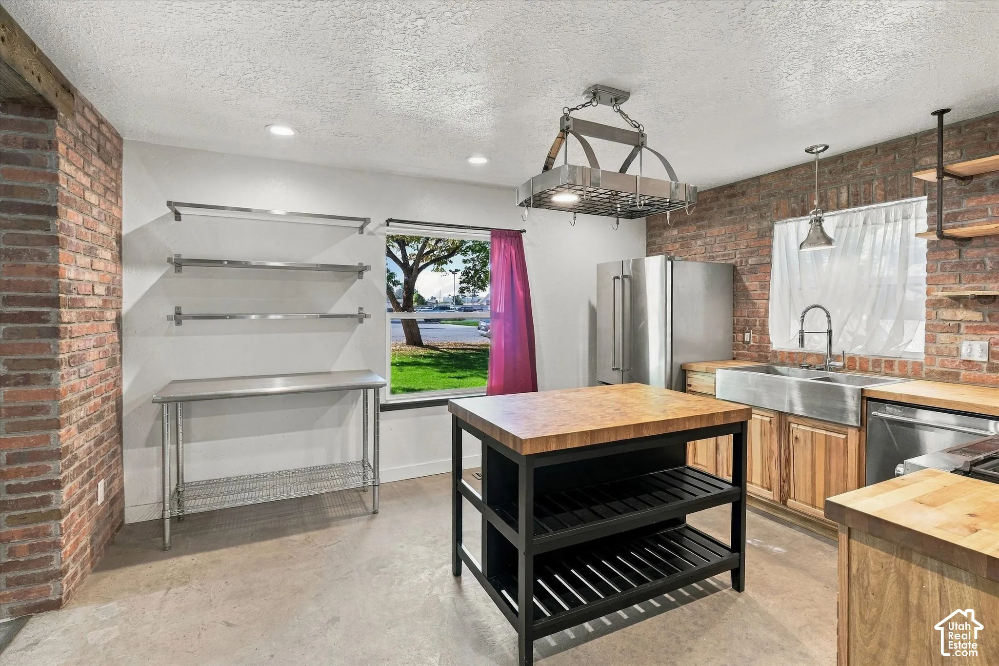Exposed brick accents, a stainless steel farmhouse sink, butcher block countertops, recessed lighting, and a pot rack with integrated lighting
