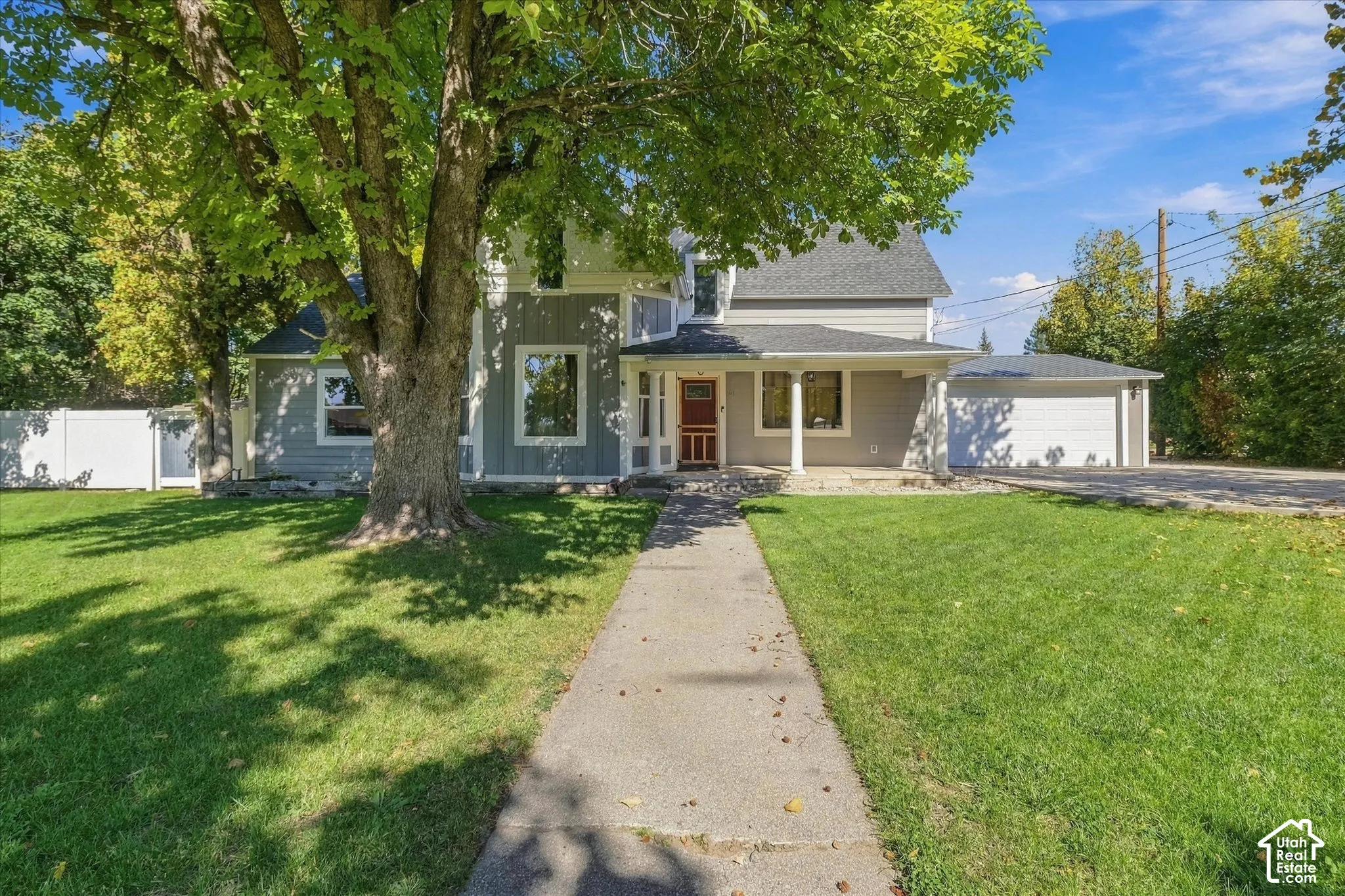 Charming residence featuring a mature shade tree anchoring the front lawn, concrete walkway leading to the entrance, and a covered front porch with classical columns