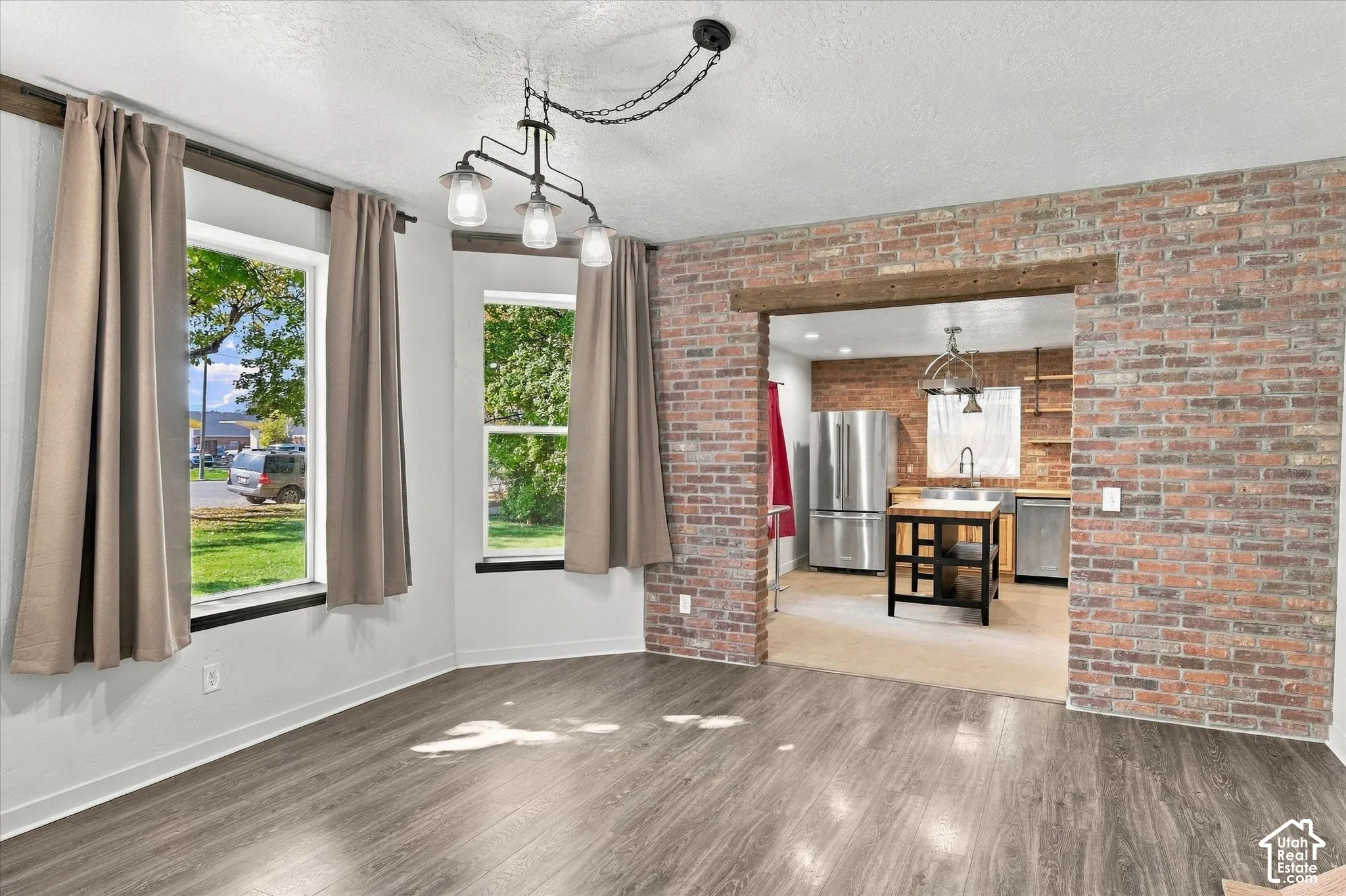 Wood-finish flooring, exposed brick accent walls, three large windows, and a multi-bulb chandelier