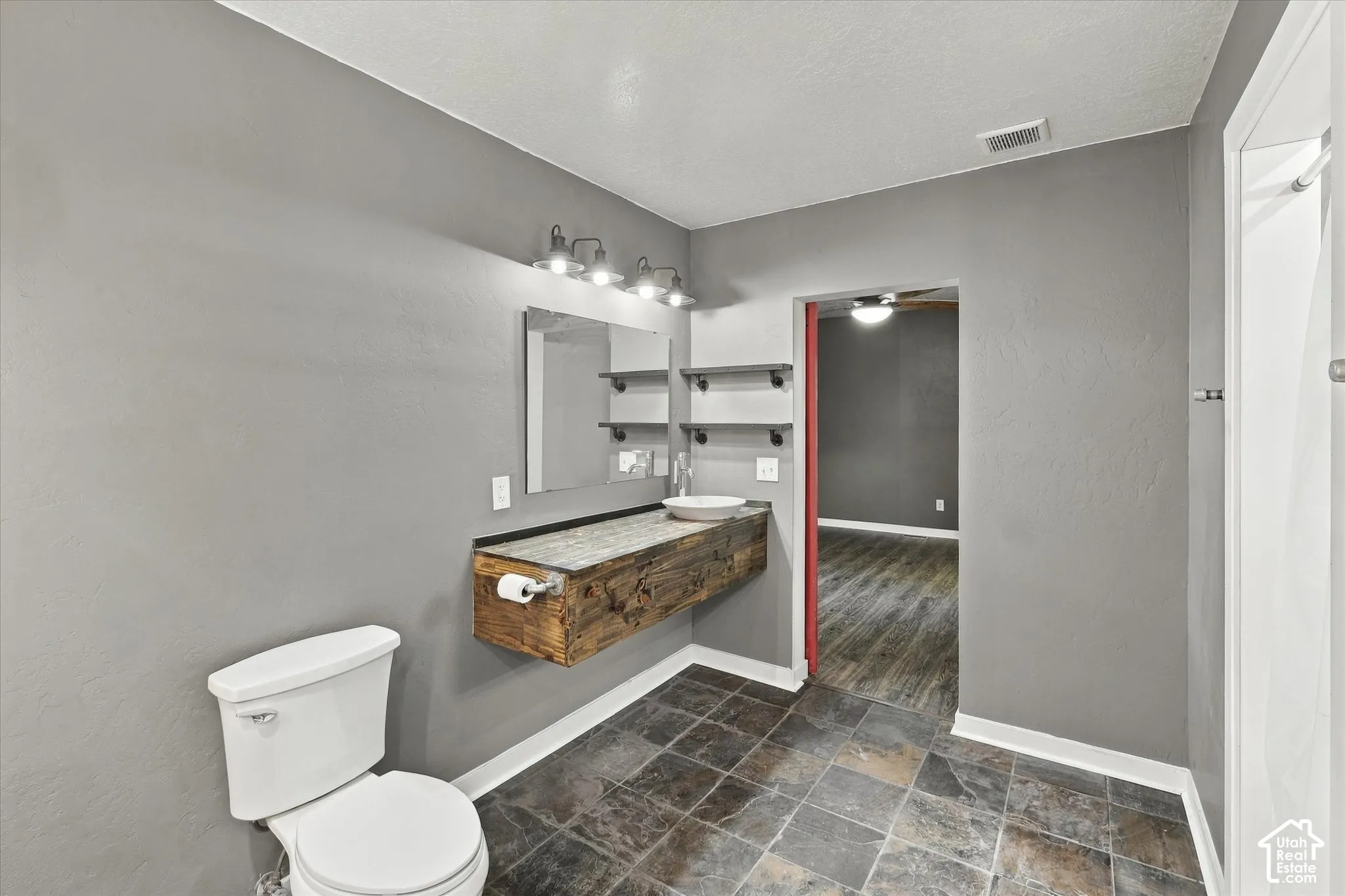 Floating rustic wood-finish vanity with a vessel sink, dark stone-look countertop, and overhead lighting fixture