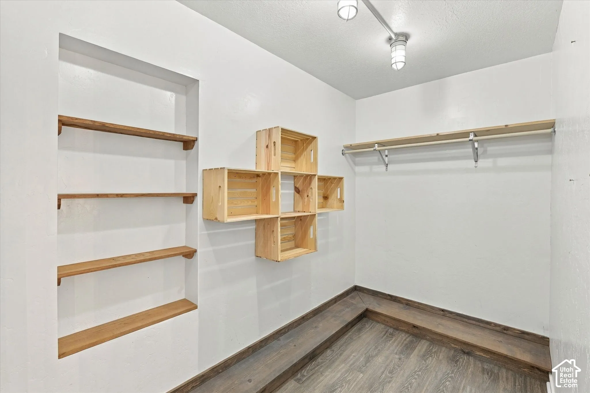 Walk-in closet featuring wood-finish floating shelving, a wall-mounted rod system, and wood-finish cubic storage cubbies