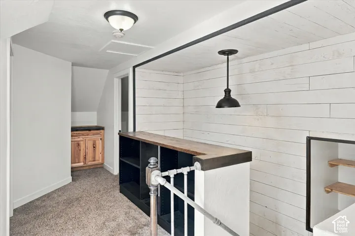 Modern finished basement featuring white subway tile walls, wood-finish countertop with black metal framing, pendant lighting, carpeted flooring, and white railing detail