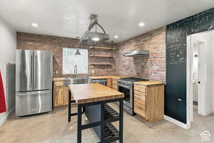 Exposed brick wall, stainless steel appliances, wood-finish countertops, central island, and open shelving