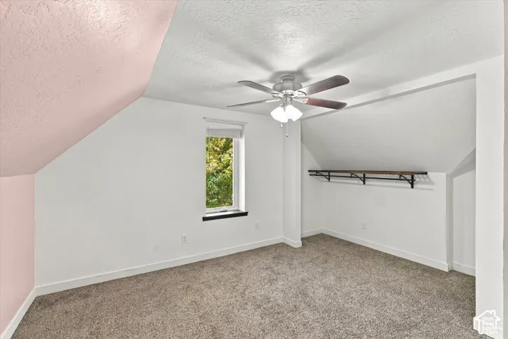 Angled ceiling, recessed window, carpeted flooring, built-in shelving, and ceiling fan with integrated lighting