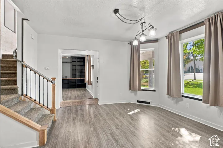 Bright, open-concept living space with wood-finish flooring, abundant natural light from multiple glass doors and windows, staircase with wooden handrail and metal balustrade, and neutral wall finishes throughout