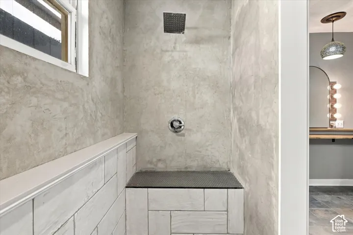 Spa-inspired walk-in shower featuring large-format stone tile walls, a rainfall showerhead with integrated body spray, frameless glass enclosure, and a built-in bench seat with contrasting dark tile