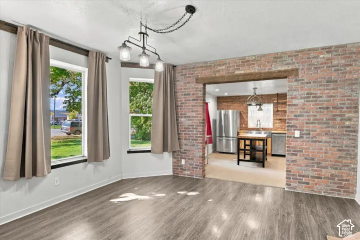Wood-finish flooring, exposed brick accent walls, three large windows, and a multi-bulb chandelier