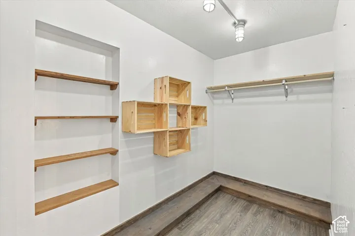 Walk-in closet featuring wood-finish floating shelving, a wall-mounted rod system, and wood-finish cubic storage cubbies