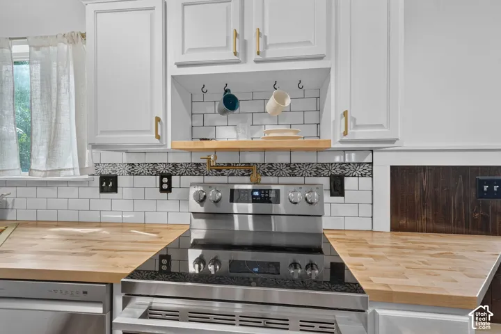 White shaker-style cabinetry with gold-tone hardware, wood-finish countertops, stainless steel range, and white subway tile backsplash with decorative accent