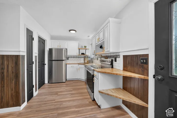White cabinetry with gold-tone hardware, wood-finish flooring, stainless steel appliances, white subway tile backsplash, and wood countertops with built-in shelving