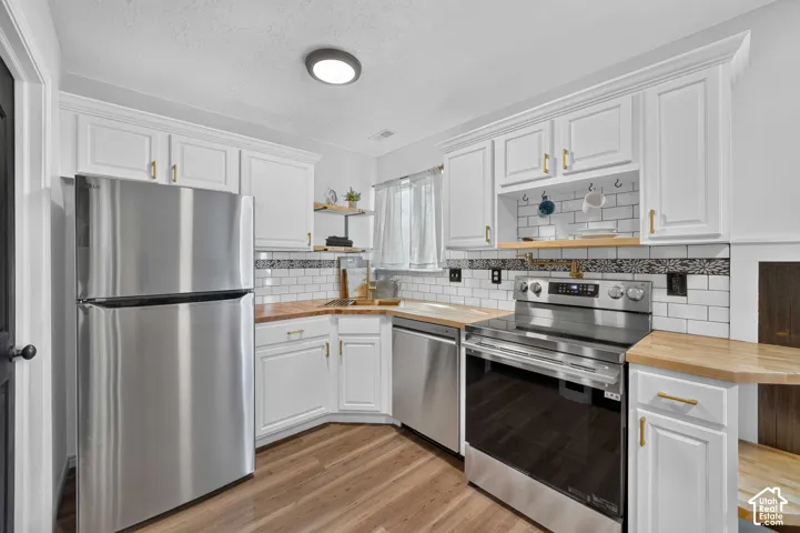 Kitchen featuring white cabinetry with gold-finish hardware, wood-finish countertops, subway tile backsplash, and stainless steel appliances
