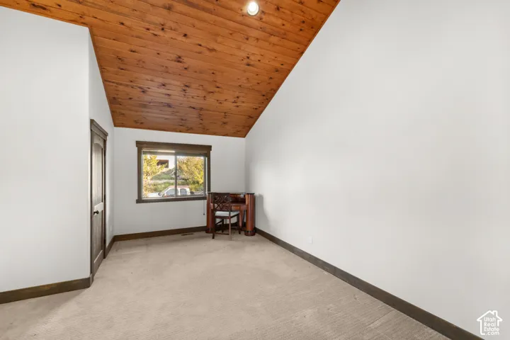 Vaulted wood-paneled ceiling with recessed lighting, light-colored carpeting, and a framed window