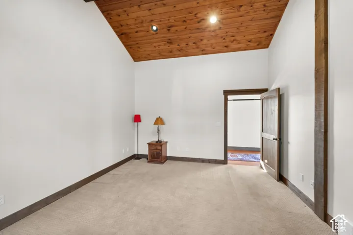 Vaulted wood-paneled ceiling, white walls, carpeted flooring, wood-finish door, and wood-finish trim