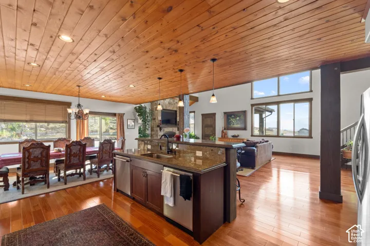 Wood-plank ceiling with recessed lighting, wood-finish flooring, stone-clad fireplace, kitchen island with integrated sink, and large windows