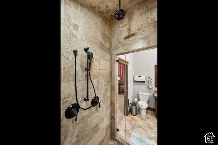 Walk-in shower with full-height tile surround, matte black rain shower head, and an adjustable handheld shower fixture