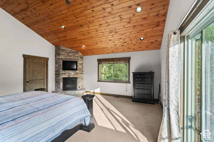 Vaulted wood-paneled ceiling with recessed lighting, stone-clad fireplace, and sliding glass door