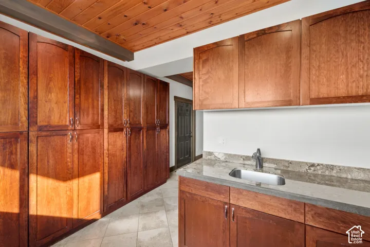 Wood-finish cabinetry, stone countertop, stainless steel sink, wood-paneled ceiling, and tiled flooring