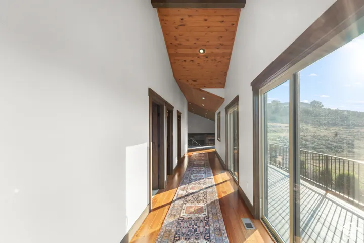 Hardwood flooring throughout, a wood-paneled angled ceiling with recessed lighting, and multiple sliding glass doors leading to an exterior balcony with metal railings