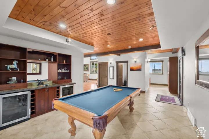 Built-in wet bar with wood cabinetry and undercounter refrigeration, wood plank ceiling, exposed wood beams, and tiled flooring