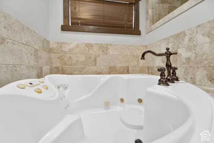 Jetted soaking tub with a bronze-finish faucet, surrounded by natural stone-look wall tiling