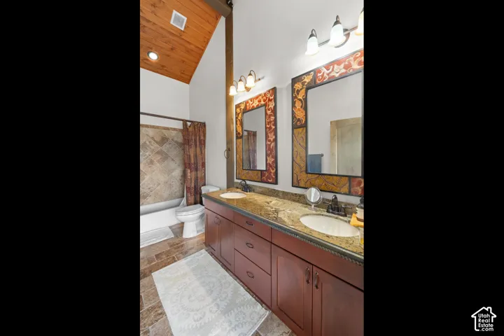 Vaulted wood-paneled ceiling, wood-finish flooring, dual vanity with undermount sinks, stone countertops, and tiled bath surround