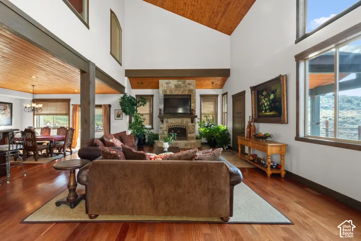 Vaulted ceilings with wood-paneled accents, stone fireplace, hardwood flooring, large windows, and exposed wood beams
